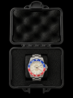 A stainless steel wristwatch with a silver-tone metal bracelet and a distinctive red, white, and blue bezel sits inside an open black protective case with black foam padding, set against a solid black background.