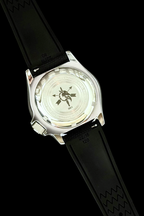 Close-up of the back of a wristwatch with a silver-toned metal case and a black strap, photographed against a solid black background.