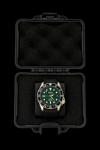 A wristwatch with a green dial and black bezel, displayed inside an open black protective case on a black background.